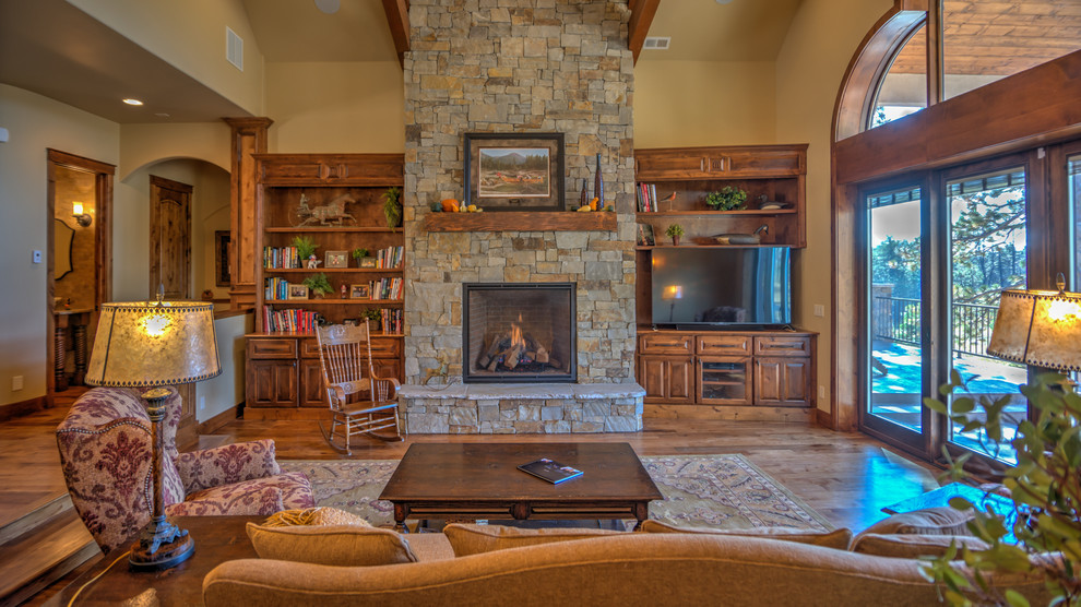 Example of a large mountain style formal and open concept medium tone wood floor living room design in Denver with beige walls, a standard fireplace, a stone fireplace and a tv stand