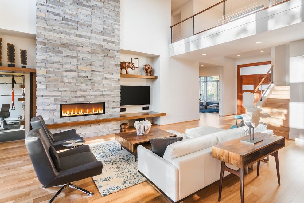 Modernes Wohnzimmer mit weißer Wandfarbe, braunem Holzboden, Gaskamin, Kaminumrandung aus Stein, TV-Wand und braunem Boden in Los Angeles