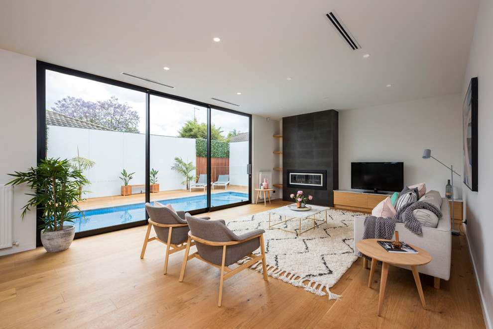 Offenes Modernes Wohnzimmer mit weißer Wandfarbe, braunem Holzboden, Gaskamin, Kaminumrandung aus Metall und freistehendem TV in Melbourne