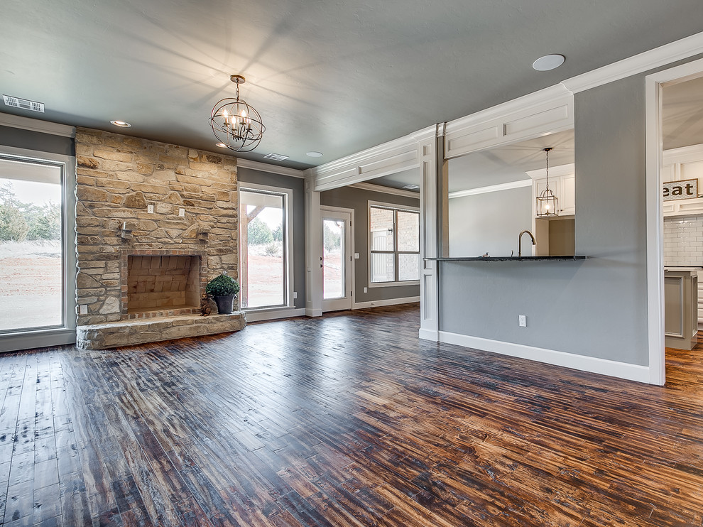 Großes, Offenes Country Wohnzimmer mit grauer Wandfarbe, braunem Holzboden, Kamin, Kaminumrandung aus Stein und TV-Wand in Oklahoma City
