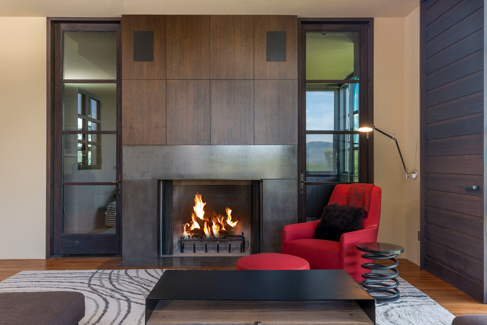 Réalisation d'un grand salon design ouvert avec un sol en bois brun, une cheminée standard, un téléviseur dissimulé, un mur beige et un manteau de cheminée en béton.
