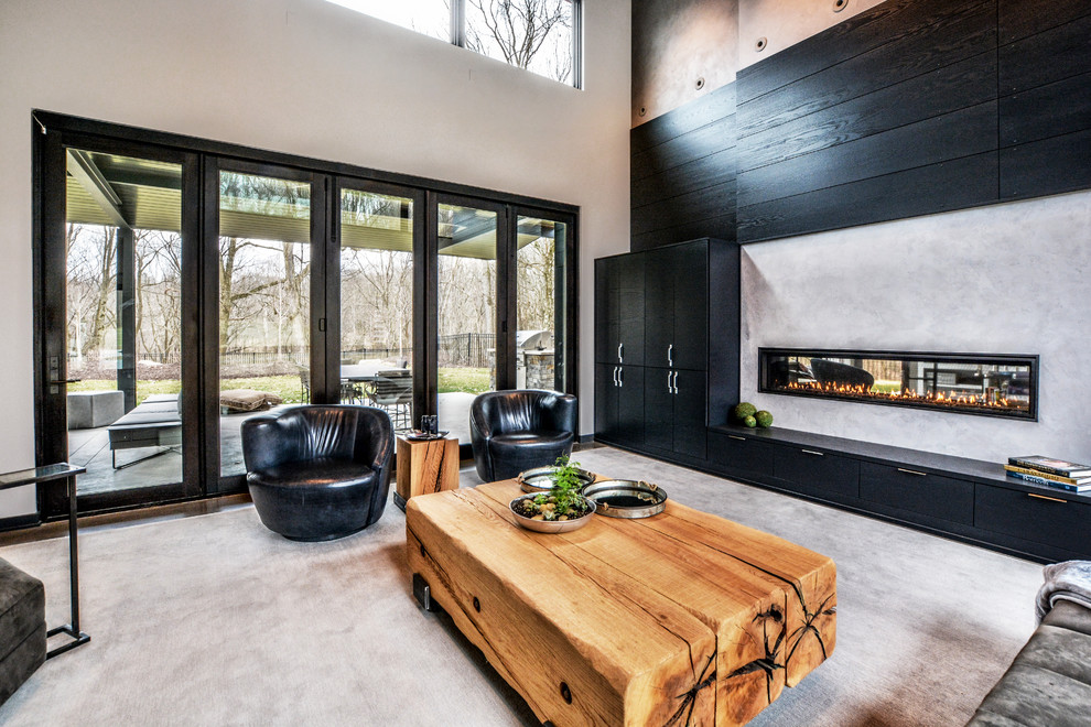 Foto di un ampio soggiorno moderno aperto con pareti grigie, pavimento in cemento, camino bifacciale, cornice del camino in legno e TV nascosta