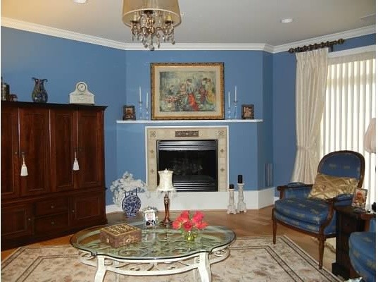 Ejemplo de salón para visitas abierto clásico de tamaño medio con paredes azules, suelo de madera clara, chimenea de esquina, marco de chimenea de piedra y televisor retractable