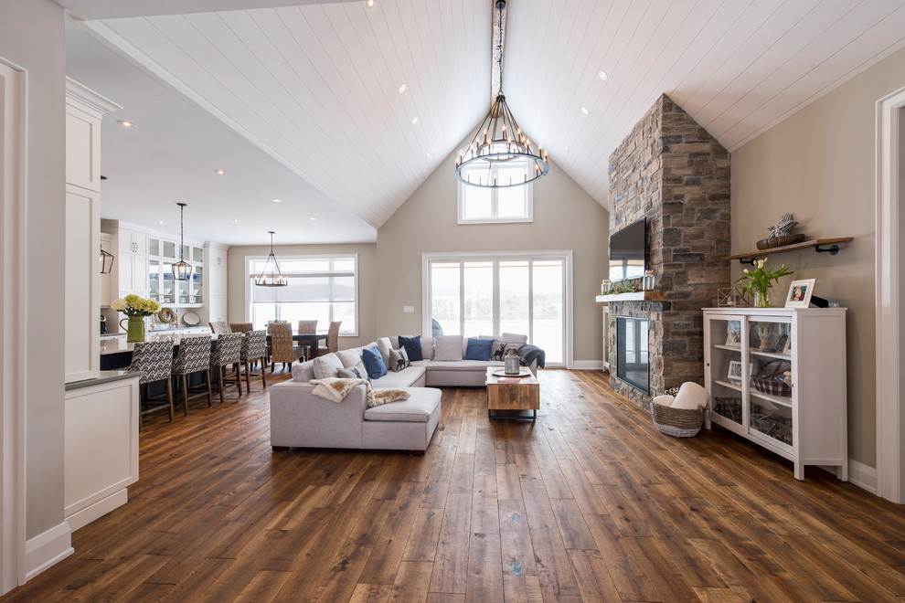 Inspiration for a huge transitional open concept medium tone wood floor and brown floor living room remodel in Toronto with gray walls, a standard fireplace, a stone fireplace and a wall-mounted tv