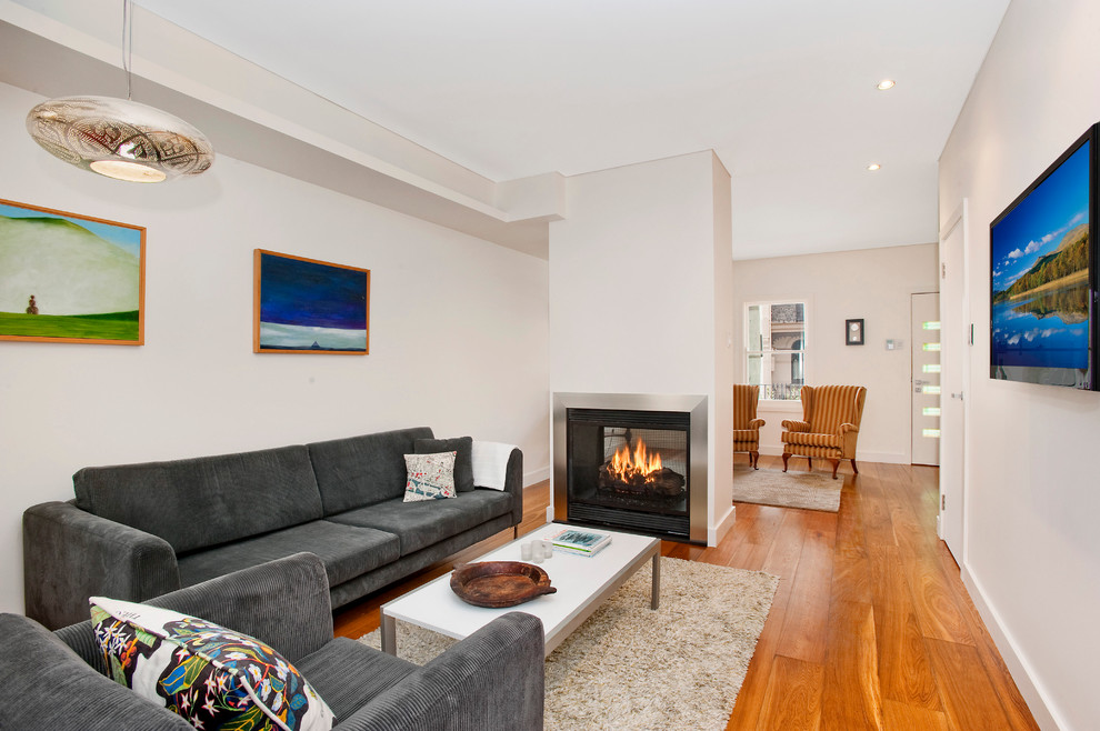Offenes Modernes Wohnzimmer mit beiger Wandfarbe, braunem Holzboden, Tunnelkamin, Kaminumrandung aus Metall und TV-Wand in Sydney