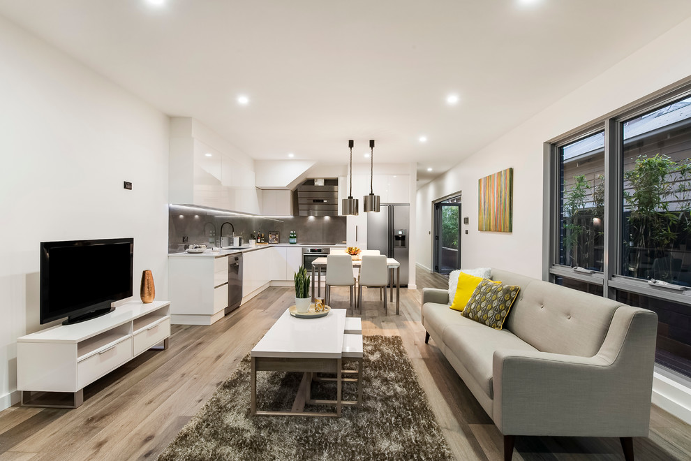 Стильный дизайн: открытая гостиная комната в современном стиле с белыми стенами, светлым паркетным полом и отдельно стоящим телевизором - последний тренд