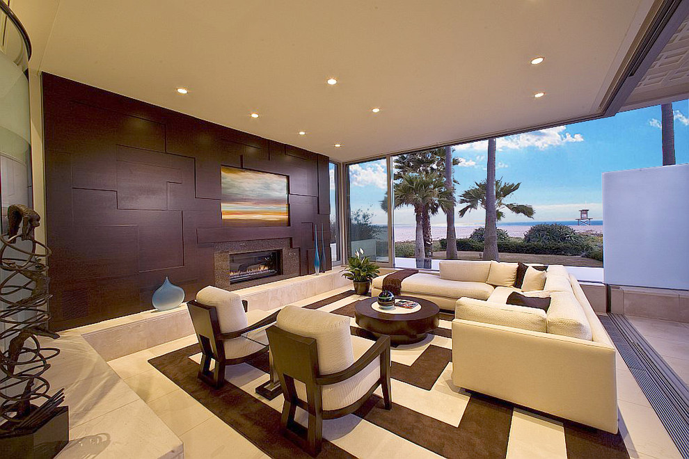 На фото: большая открытая гостиная комната в современном стиле с белыми стенами, полом из известняка, горизонтальным камином, фасадом камина из дерева и скрытым телевизором с