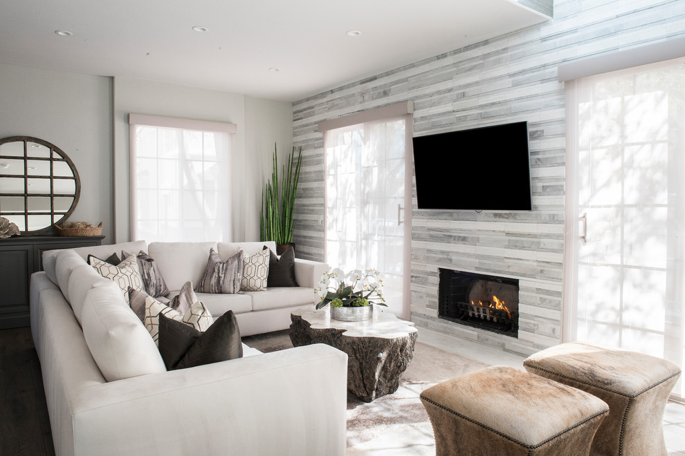 Foto de salón actual con paredes grises, suelo de madera oscura, marco de chimenea de piedra y televisor colgado en la pared