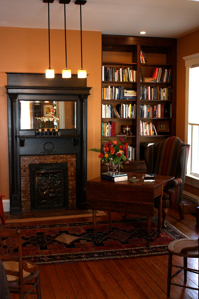 Exempel på ett litet eklektiskt separat vardagsrum, med ett bibliotek, orange väggar, mellanmörkt trägolv, en standard öppen spis och en spiselkrans i trä