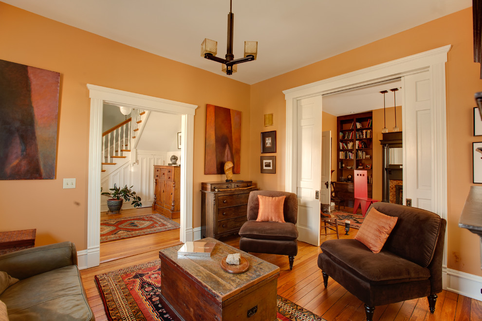 Inspiration för små eklektiska separata vardagsrum, med ett bibliotek, orange väggar, mellanmörkt trägolv, en standard öppen spis och en spiselkrans i trä