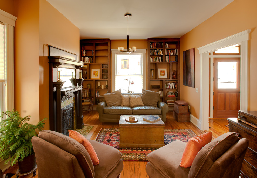 Idée de décoration pour un petit salon bohème fermé avec une bibliothèque ou un coin lecture, un mur orange, un sol en bois brun, une cheminée standard, un manteau de cheminée en carrelage et aucun téléviseur.