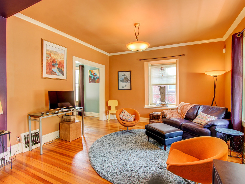 Cette image montre un salon victorien de taille moyenne avec un mur orange, un sol en bois brun et un téléviseur indépendant.