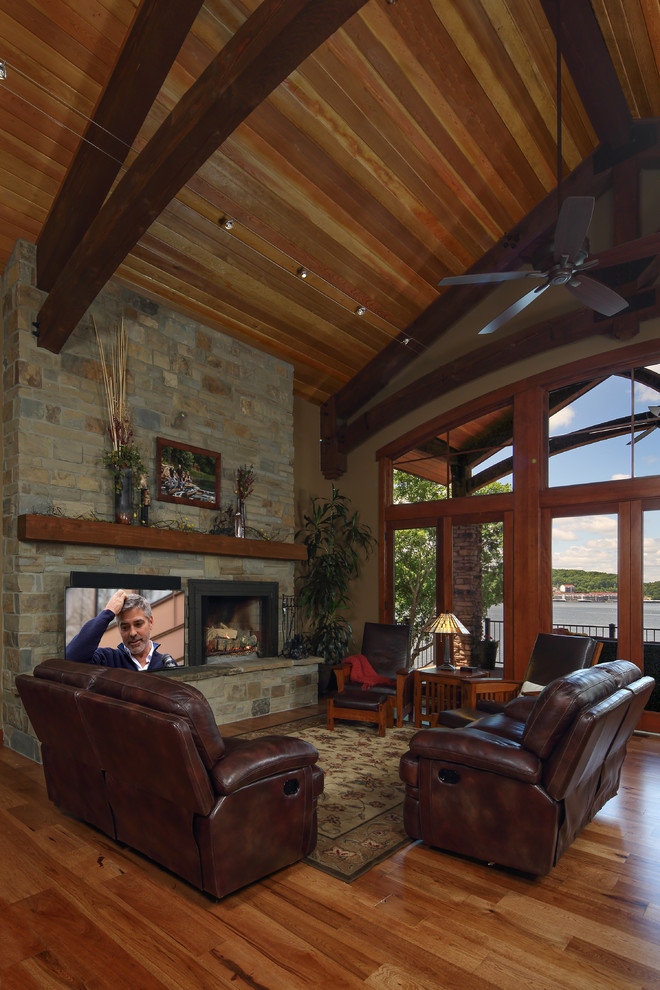 Aménagement d'un grand salon craftsman ouvert avec un mur marron, un sol en bois brun, une cheminée standard, un manteau de cheminée en pierre, un téléviseur indépendant et un sol marron.