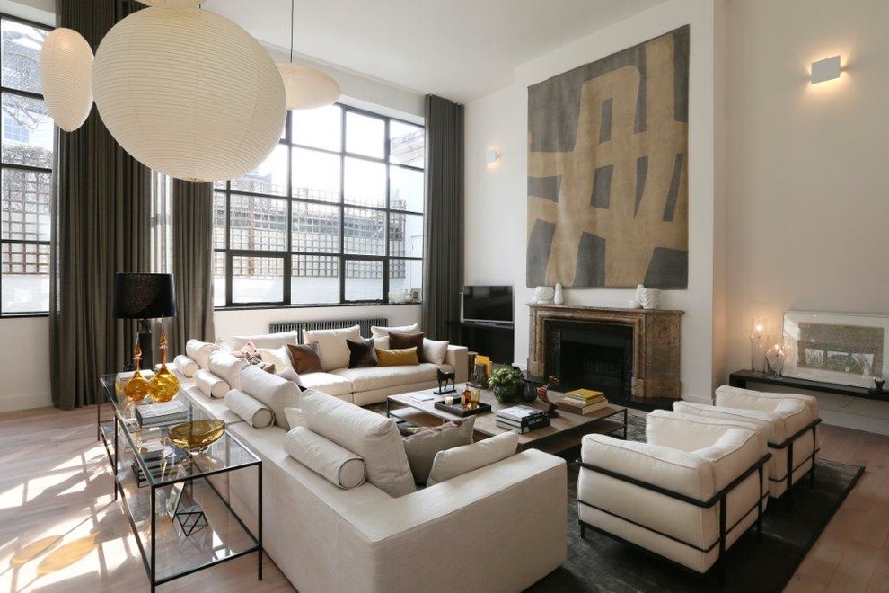 ニューヨークにある広いコンテンポラリースタイルのおしゃれなLDK (白い壁、淡色無垢フローリング、標準型暖炉、石材の暖炉まわり、据え置き型テレビ、茶色い床) の写真