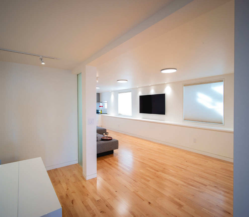 Foto på ett litet funkis allrum med öppen planlösning, med mellanmörkt trägolv, vita väggar, en väggmonterad TV och brunt golv