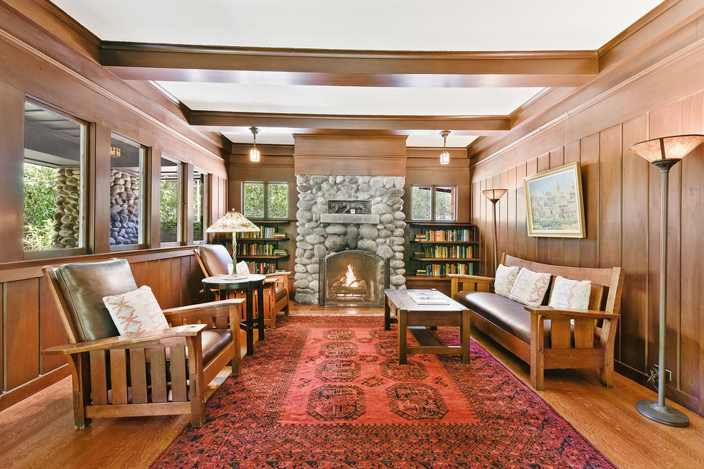 Inspiration för stora amerikanska vardagsrum, med en standard öppen spis, en spiselkrans i sten, ett bibliotek, bruna väggar och mellanmörkt trägolv