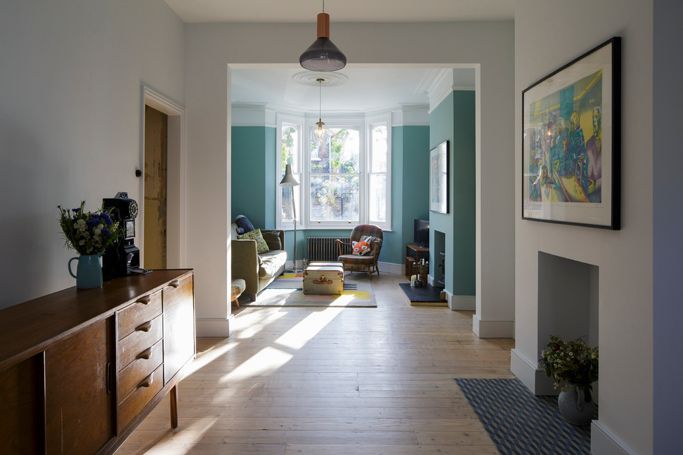 Imagen de salón abierto actual de tamaño medio con paredes azules, suelo de madera clara, todas las chimeneas, marco de chimenea de yeso y televisor independiente