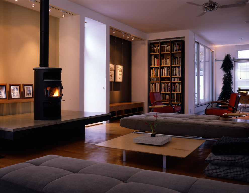 Cette image montre un salon mansardé ou avec mezzanine traditionnel de taille moyenne avec un mur multicolore, un sol en bois brun, un poêle à bois, un manteau de cheminée en béton et un téléviseur dissimulé.