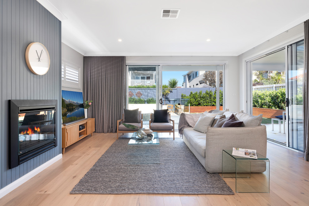 Example of a trendy open concept medium tone wood floor and brown floor living room design in Sydney with gray walls, a standard fireplace, a wood fireplace surround and a tv stand