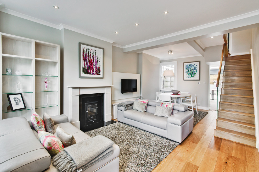 Medium sized modern open plan living room in London with grey walls, light hardwood flooring, a wood burning stove, a wooden fireplace surround and a wall mounted tv.