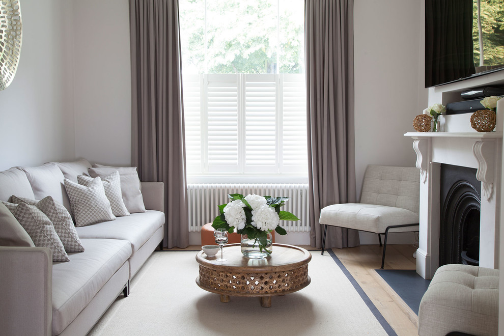 На фото: гостиная комната в стиле неоклассика (современная классика) с белыми стенами, светлым паркетным полом, стандартным камином и телевизором на стене