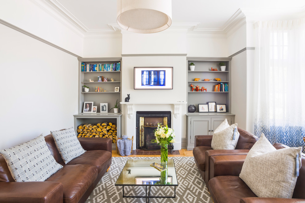 На фото: изолированная гостиная комната среднего размера в викторианском стиле с серыми стенами, светлым паркетным полом, печью-буржуйкой, фасадом камина из плитки, телевизором на стене и коричневым полом с