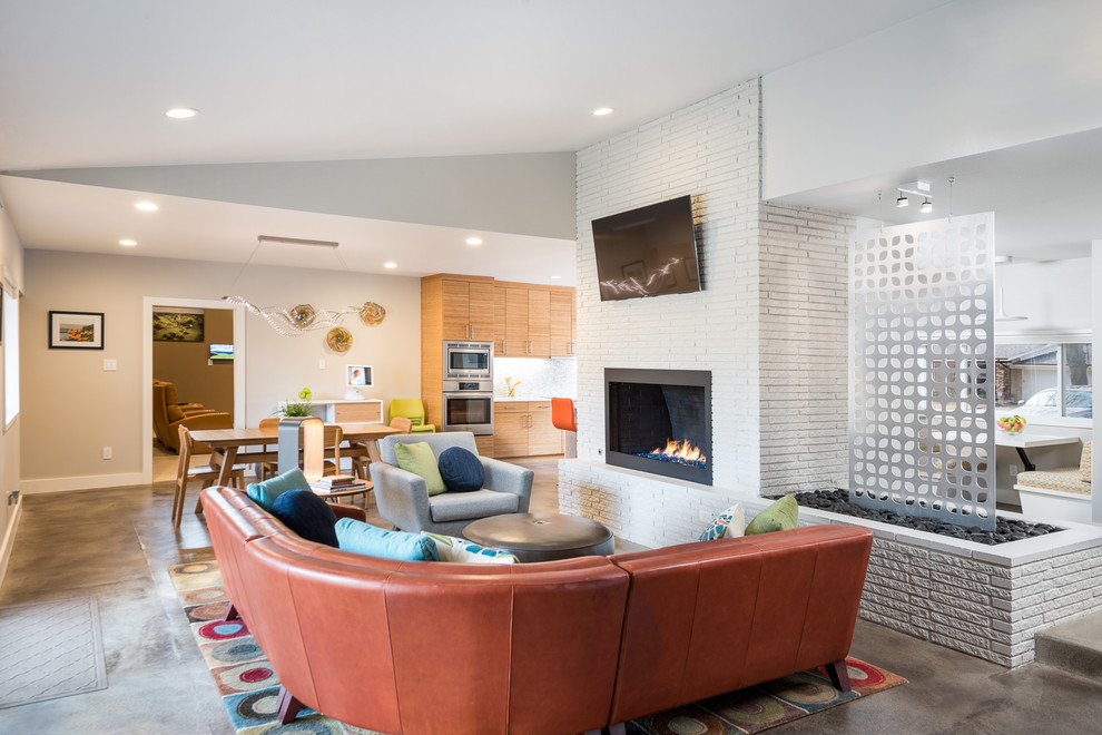 Стильный дизайн: открытая гостиная комната в стиле ретро с белыми стенами, бетонным полом, стандартным камином, фасадом камина из кирпича, телевизором на стене и серым полом - последний тренд