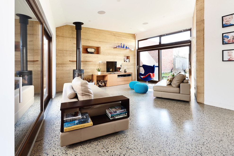 Modelo de salón abierto actual de tamaño medio con suelo de cemento, paredes blancas, estufa de leña y televisor independiente