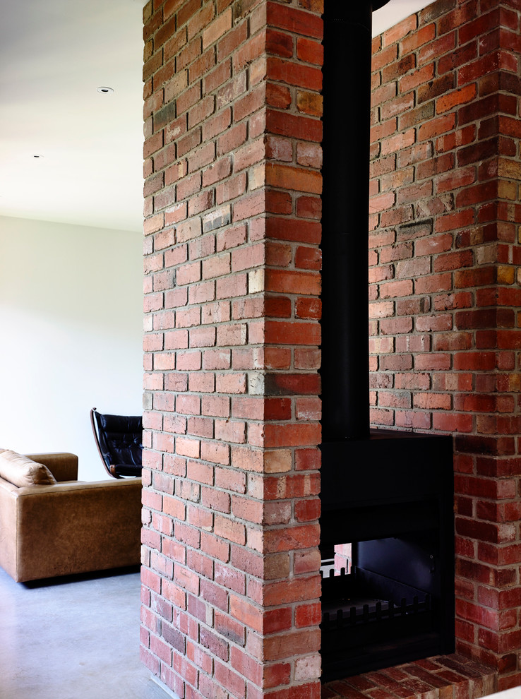 Example of a mid-sized trendy open concept concrete floor living room library design in Melbourne with white walls, a two-sided fireplace, a brick fireplace and a concealed tv