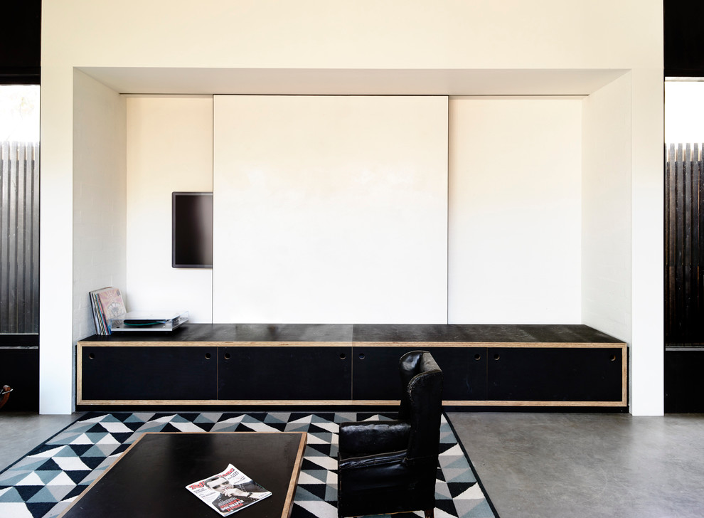 Immagine di un soggiorno design di medie dimensioni con libreria, pareti bianche, pavimento in cemento, camino bifacciale, cornice del camino in mattoni e TV nascosta