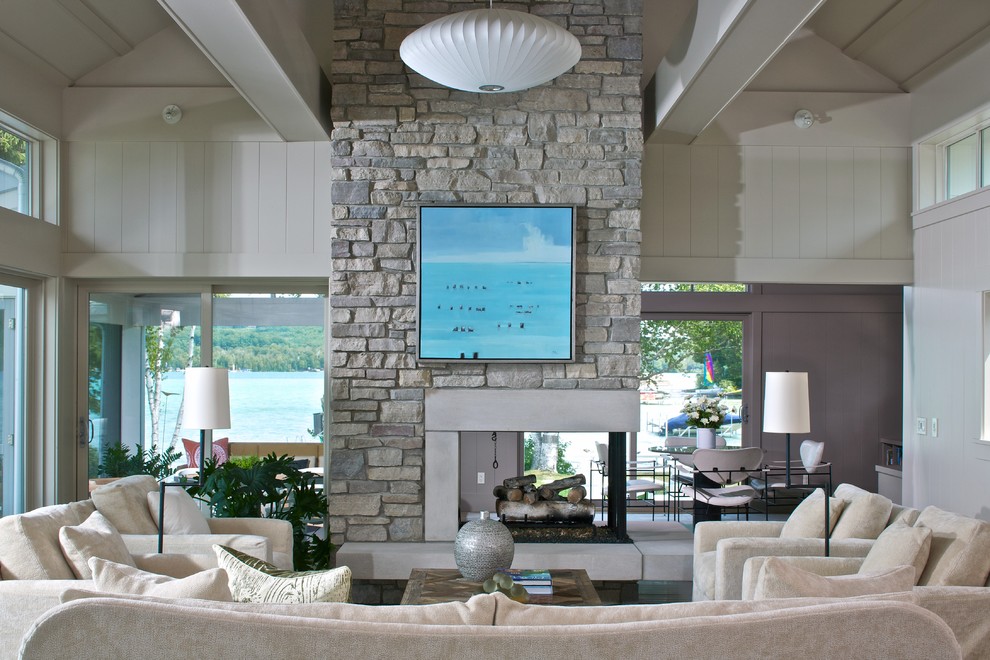 Idée de décoration pour un salon design ouvert avec une cheminée double-face, un manteau de cheminée en pierre, un mur blanc et éclairage.