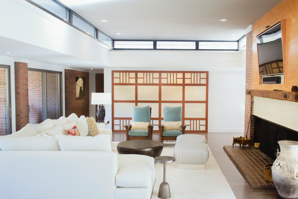 На фото: большая парадная, изолированная гостиная комната в стиле модернизм с белыми стенами, паркетным полом среднего тона, стандартным камином, фасадом камина из кирпича, телевизором на стене и серым полом с