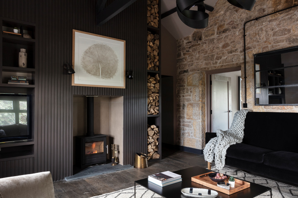 Cette image montre un grand salon design fermé avec un mur noir, parquet foncé, un poêle à bois, un manteau de cheminée en bois, un téléviseur fixé au mur et un sol gris.