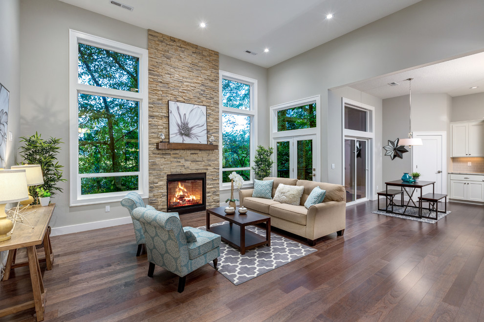 Cette image montre un grand salon design ouvert avec un mur gris, un sol en bois brun, une cheminée standard, un manteau de cheminée en brique et un sol marron.