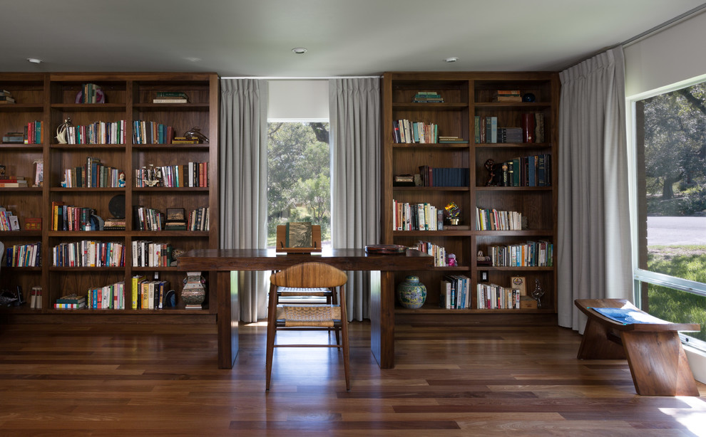 Foto på ett stort funkis vardagsrum, med ett bibliotek, vita väggar, mörkt trägolv, en standard öppen spis och en spiselkrans i tegelsten