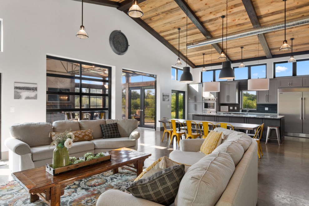 This is an example of a large industrial open plan living room in Milwaukee with white walls, concrete flooring, a standard fireplace, a built-in media unit, brown floors and a vaulted ceiling.