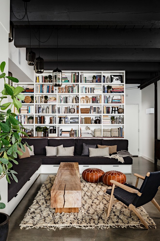 Foto på ett industriellt vardagsrum, med ett bibliotek och betonggolv