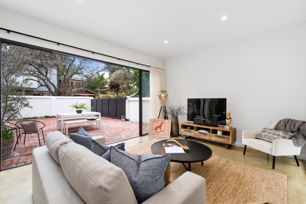 Offenes Landhausstil Wohnzimmer mit weißer Wandfarbe, Betonboden, freistehendem TV und gelbem Boden