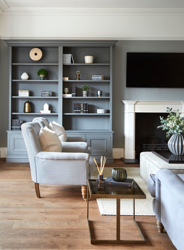 Идея дизайна: гостиная комната в стиле неоклассика (современная классика) с с книжными шкафами и полками, серыми стенами, паркетным полом среднего тона, стандартным камином, телевизором на стене и коричневым полом