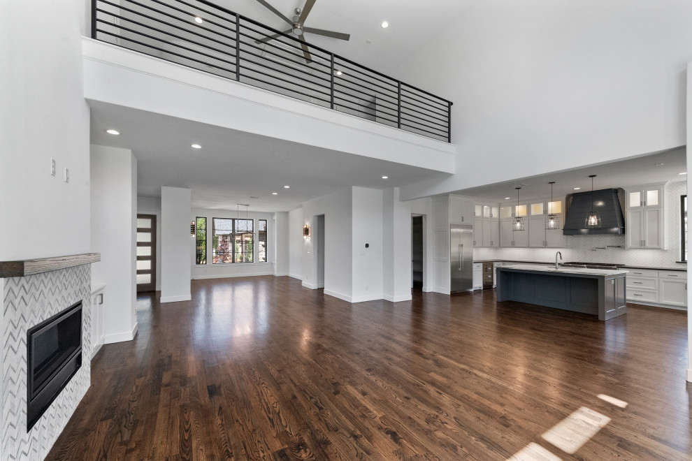 Expansive contemporary open plan living room in Dallas with white walls, medium hardwood flooring, a standard fireplace, a tiled fireplace surround, a wall mounted tv and brown floors.