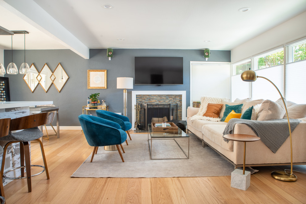 Cette image montre un salon traditionnel ouvert avec un mur bleu, un sol en bois brun, une cheminée standard, un manteau de cheminée en pierre de parement, un téléviseur fixé au mur et un sol marron.