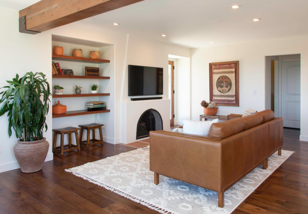 Example of a southwest open concept medium tone wood floor and brown floor living room design in San Diego with a concrete fireplace, white walls, a standard fireplace and a wall-mounted tv