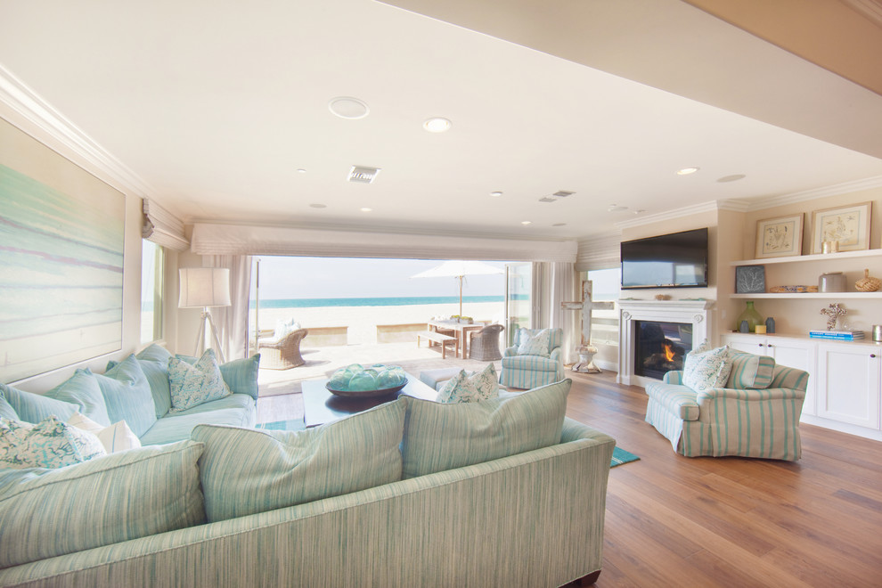 Стильный дизайн: большая открытая гостиная комната в морском стиле с бежевыми стенами, светлым паркетным полом, стандартным камином, фасадом камина из дерева и телевизором на стене - последний тренд