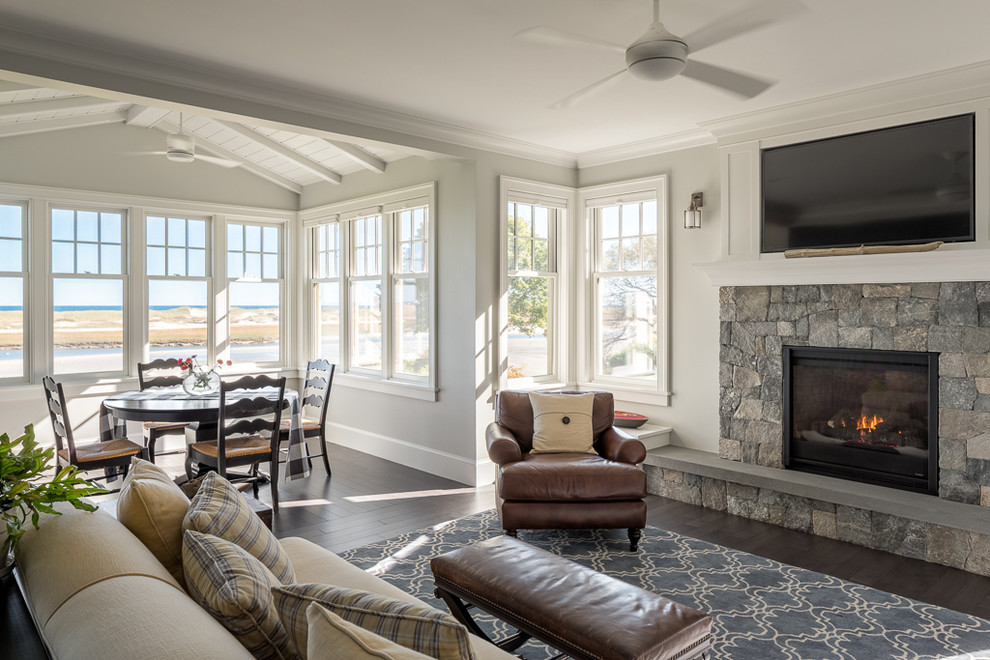 Offenes Maritimes Wohnzimmer mit beiger Wandfarbe, dunklem Holzboden, Kamin, Kaminumrandung aus Stein und TV-Wand in Portland Maine