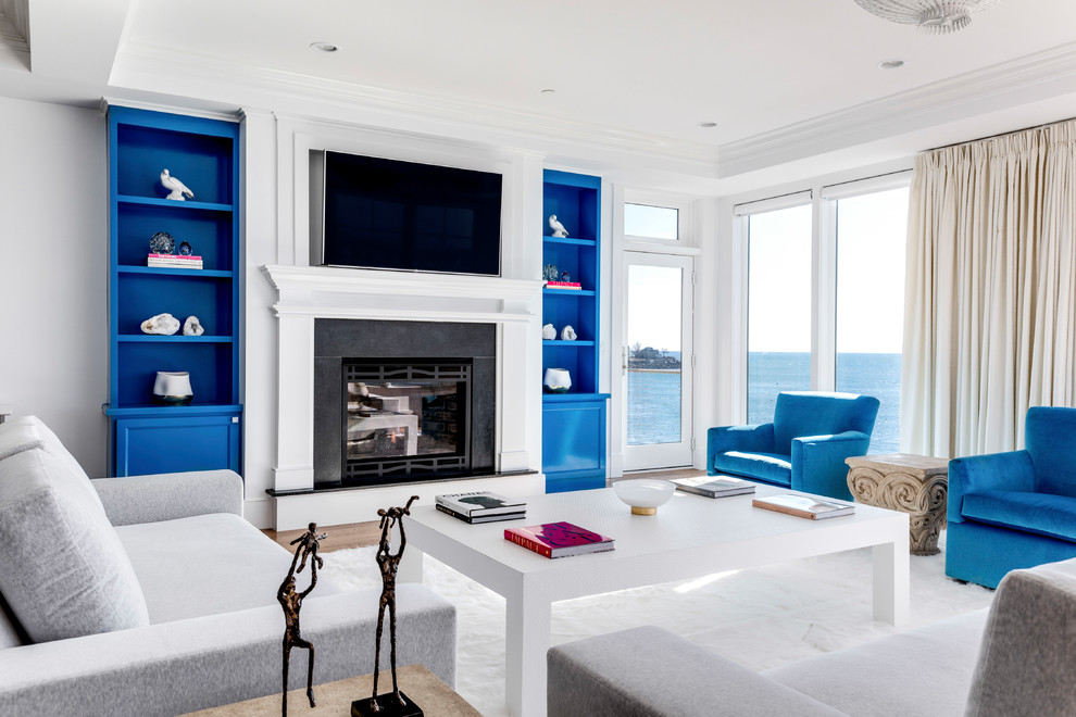 ボストンにある高級な広いビーチスタイルのおしゃれなリビング (白い壁、無垢フローリング、標準型暖炉、木材の暖炉まわり、壁掛け型テレビ、白い床) の写真