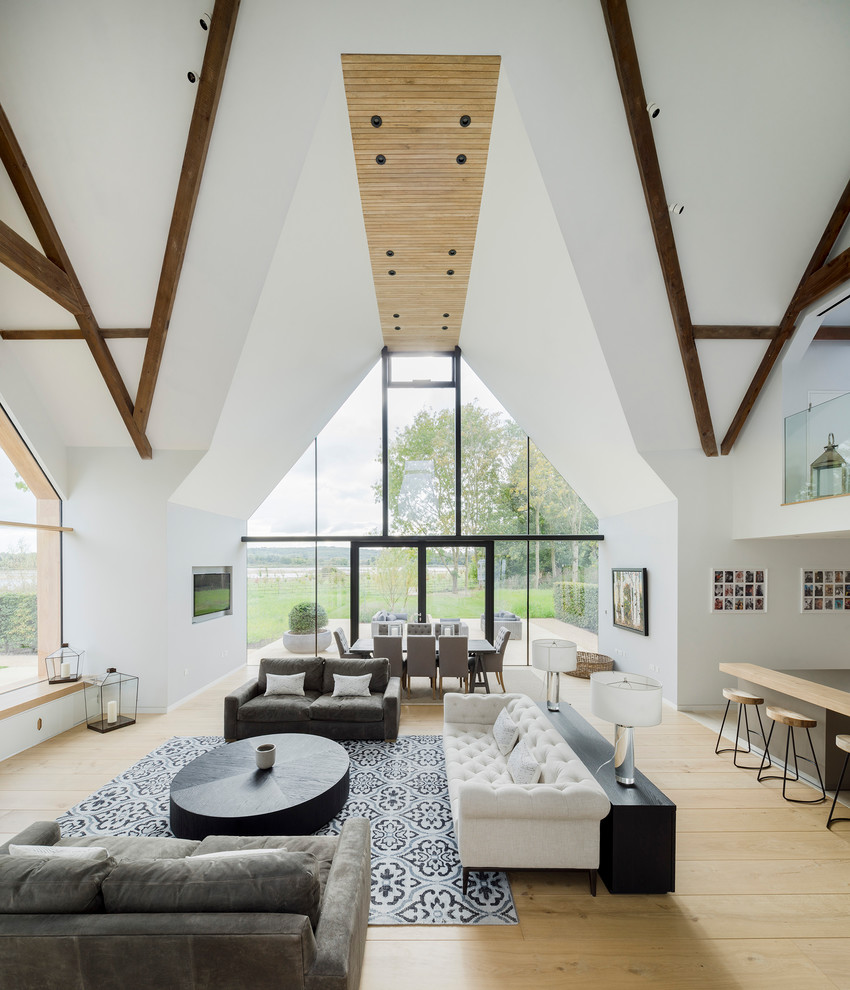 This is an example of a large farmhouse open plan living room in Wiltshire with white walls, light hardwood flooring, a wall mounted tv and beige floors.