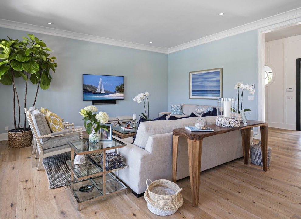 На фото: большая открытая гостиная комната в морском стиле с синими стенами, паркетным полом среднего тона и телевизором на стене с