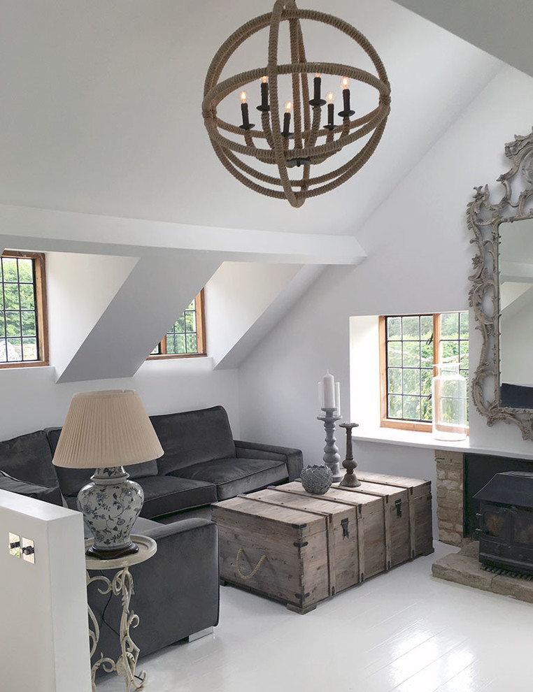 Modelo de salón abierto de estilo de casa de campo grande con suelo de madera pintada, estufa de leña, marco de chimenea de ladrillo y paredes blancas
