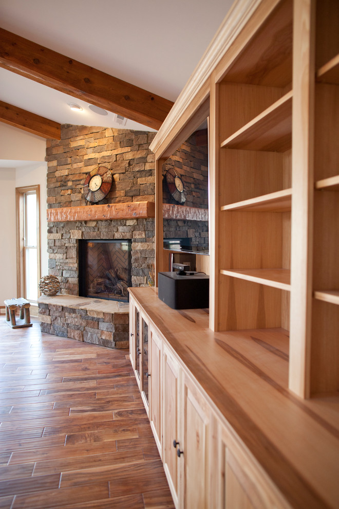 Cette image montre un grand salon ouvert avec un sol en bois brun, une cheminée d'angle, un manteau de cheminée en pierre et un téléviseur encastré.