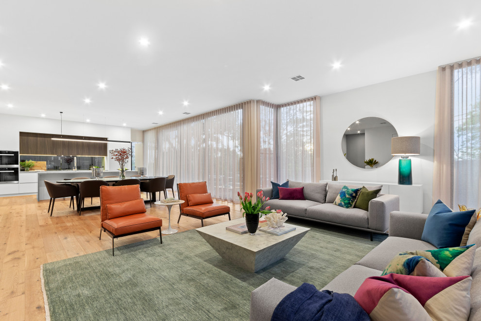 This is an example of a large contemporary formal open plan living room in Melbourne with white walls, light hardwood flooring, no fireplace, a freestanding tv and brown floors.
